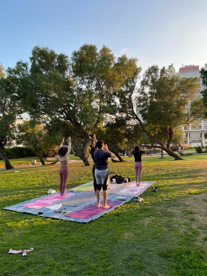 A group of adults practicing yoga outdoors on a sunny day in an Israeli park.